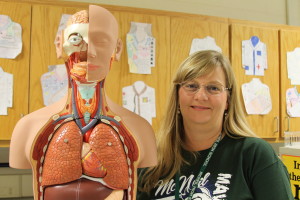 Hart-Sobkowiak strikes a pose next to an anatomical diagram in her classroom.  
