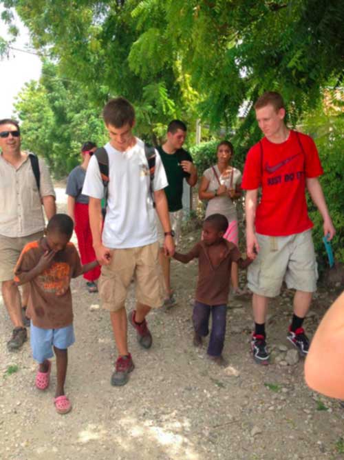 Sophomore Hudson Holmes (right) walking to another village hand and hand with a Haitian child
