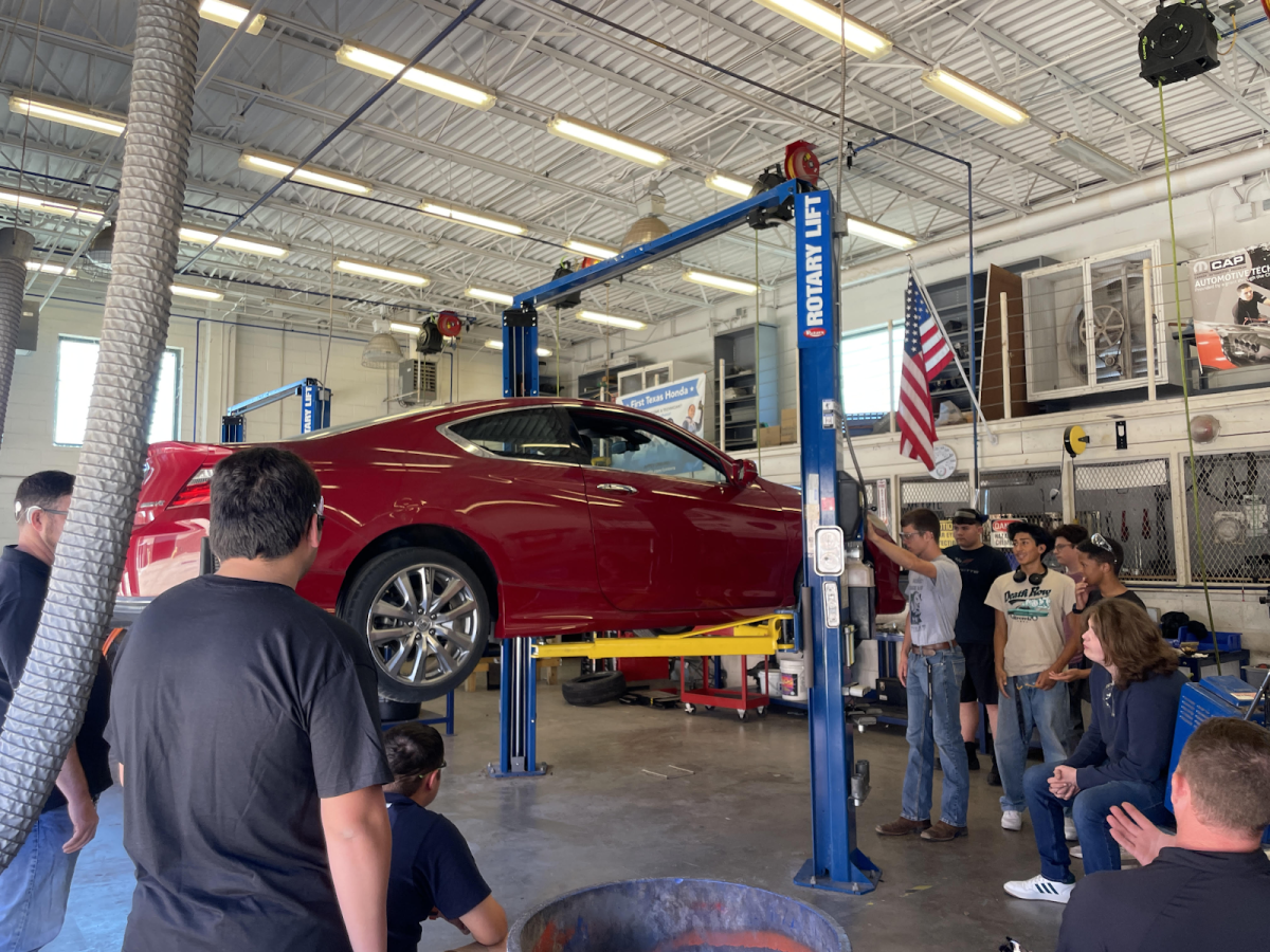 An automotive basics class uses a car lift under the watch of automotive teacher Norman Lawrence.