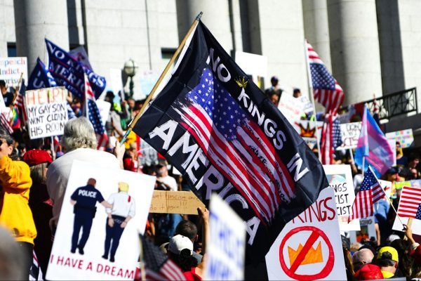 A “No Kings in America” flag waving among other signs at the ‘No Kings’ protest; Oct. 18th, 2025. Photo Courtesy of Mike Newbry / Unsplash